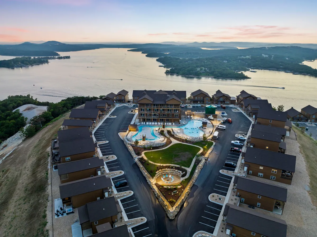 An inviting exterior view of luxurious swimming pools, manicured lawns, and the multi-story lodge set against a beautiful natural landscape. The scene exudes a tranquil yet vibrant resort atmosphere, with the pool area ready for gatherings and relaxation.