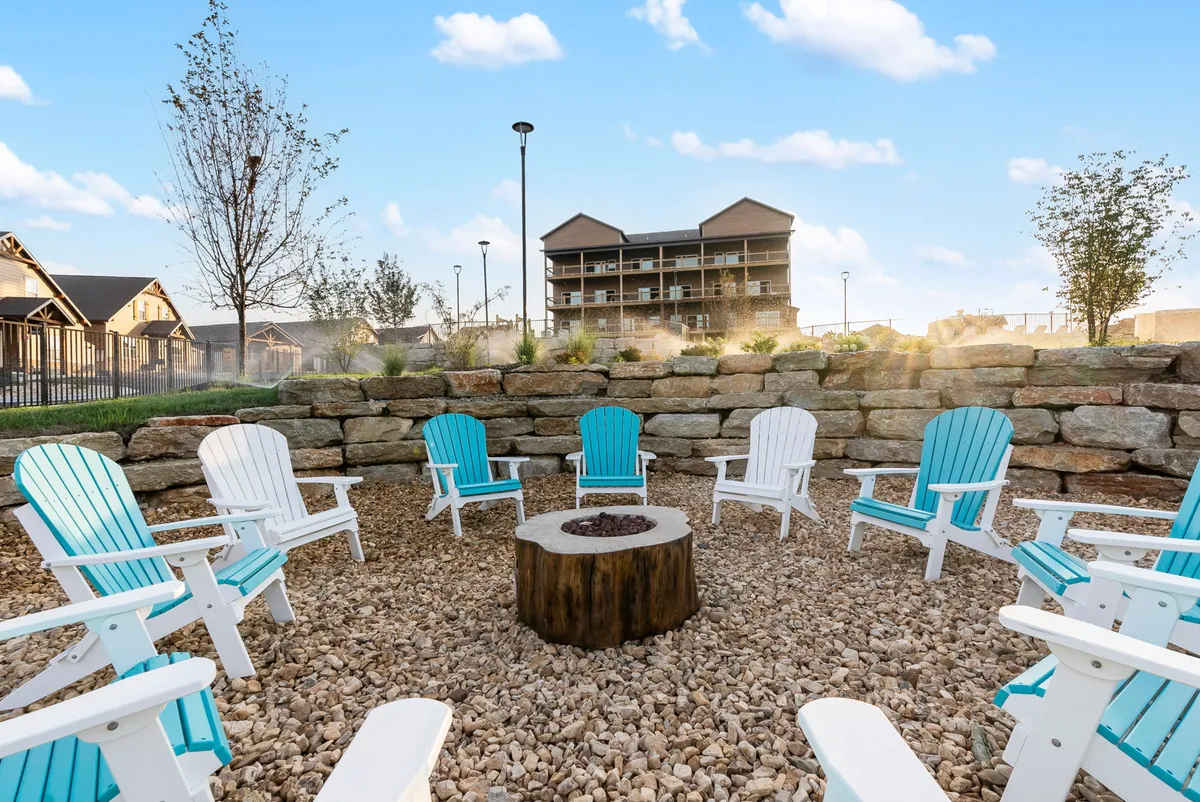 A cozy fire pit surrounded by Adirondack chairs, set against lush greenery and a stone wall. The space is designed for evening campfire gatherings, storytelling sessions, and relaxed socializing under the stars.