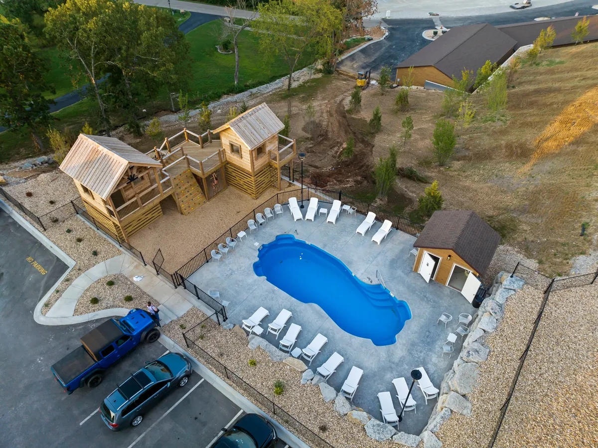 A lively outdoor resort scene featuring a swimming pool, whimsical playhouses, lounge chairs, and lush surrounding greenery. The atmosphere is playful and relaxed, ideal for children and families to gather, swim, and play.