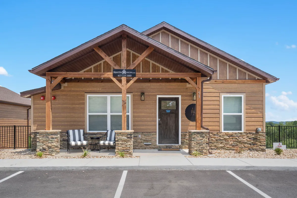 The inviting front porch of the home, featuring wooden architecture, stone accents, a welcoming front door, and comfortable seating. The porch is set up for relaxing, entertaining, and enjoying the outdoors, bridging the transition between indoor and outdoor communal spaces.