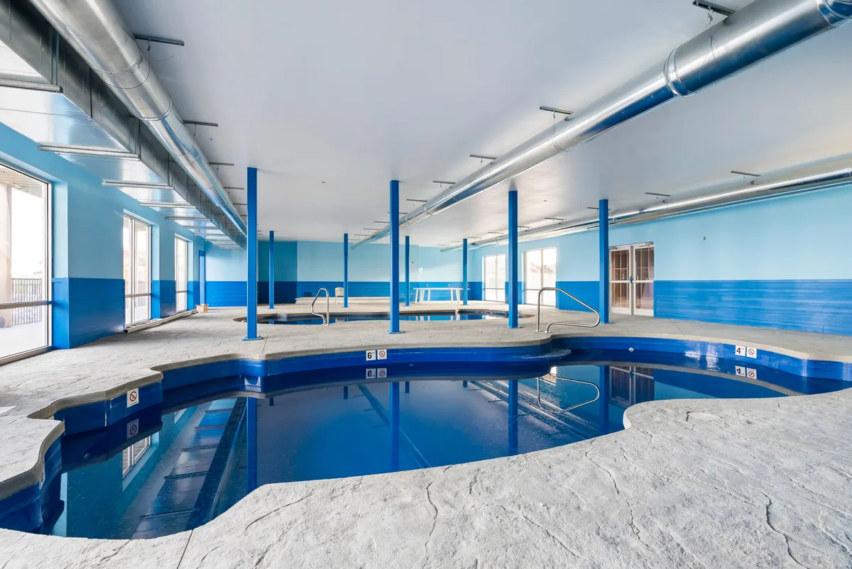 A bright and airy indoor pool area with blue walls, large windows, and supportive pillars. The space feels refreshing and inviting, perfect for year-round swimming and social activities.