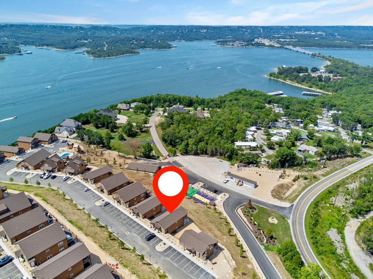 The image shows a broad view of Table Rock Lake, with houses dotting the shoreline and a parking area and road in the foreground. The scene conveys easy lake access and the vibrant setting for water activities like boating, fishing, and swimming.