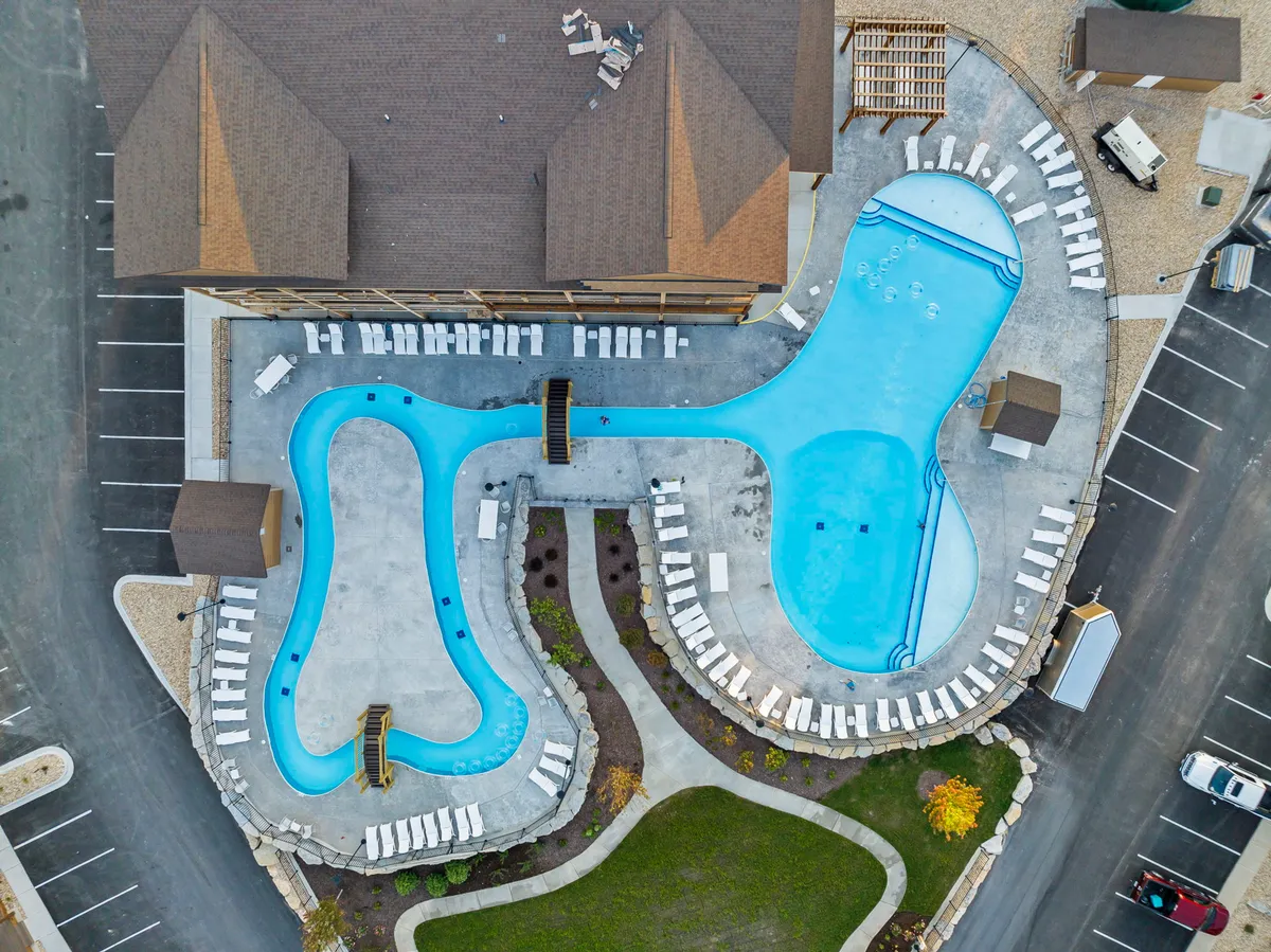 The exterior swimming pools with lounge chairs, landscaped pathways, and the encompassing building are bathed in a leisurely, welcoming light. Children are seen playing, and groups are relaxing poolside, reinforcing community and family fun.