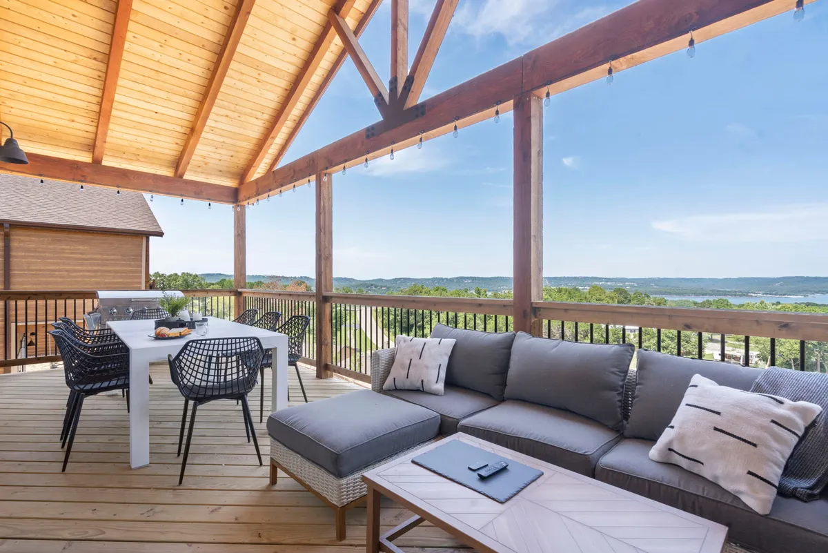A spacious deck area overlooks a sweeping landscape, featuring a comfortable seating area and a dining table with chairs. The panoramic views invite guests to enjoy sunsets, stargaze, or socialize with friends and family in a relaxed atmosphere.