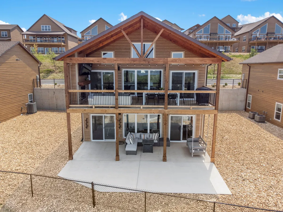 An inviting wooden deck extends from the main-level living area, furnished with comfortable outdoor seating and offering unobstructed sunset views over the lake and hills. Large windows blur the line between indoor and outdoor living, while the space is set for outdoor dining or relaxing with morning coffee.
