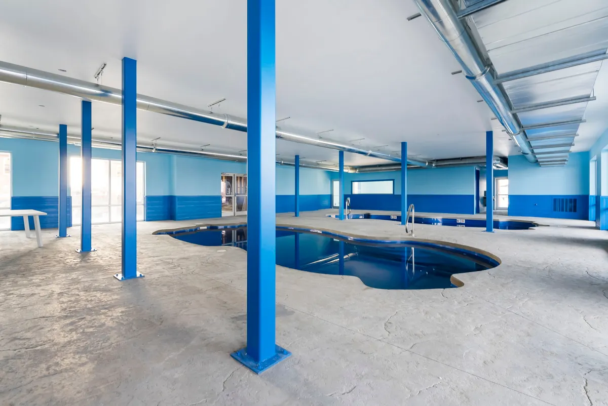 The photo captures an inviting indoor swimming pool, well-lit by large windows and accented by blue columns. The poolside area looks fresh and welcoming, ideal for all-weather swimming and relaxation.
